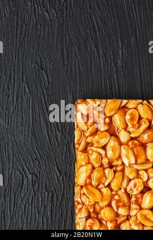 Una grande piastrella dorata di arachidi, un bar in una melassa dolce su uno sfondo di tessitura nera. Kozinaki dolci utili e gustosi dell'Est. Vista dall'alto Foto Stock