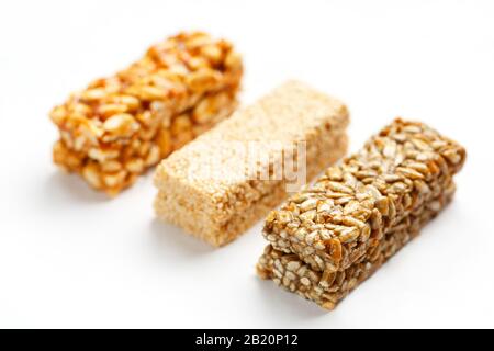 Grano granola bar con arachidi, sesamo e semi in una fila su uno sfondo bianco. Vista dall'alto Kozinaki Tre barre assortite, isolate Foto Stock