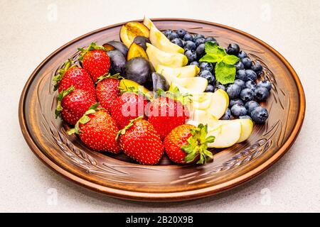 Frutti di bosco, mela, fragola, mirtillo, prugna, menta. Su piatto di ceramica etnica, sano vegetariano (vegan) concetto di cibo. Calcestruzzo di pietra Foto Stock