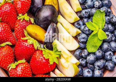 Frutti di bosco, mela, fragola, mirtillo, prugna, menta. Su piatto di ceramica etnica, sano vegetariano (vegan) concetto di cibo. Calcestruzzo di pietra Foto Stock