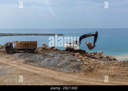 Turchia Alanya 18 aprile 2018: Un vecchio escavatore sta lavorando sulla riva del mare per prepararlo per i turisti. Un grande camion è in piedi vicino a un escavatore e wa Foto Stock