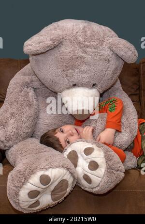 Ragazzo sorridente con orso gigante mentre si trova in grembo Foto Stock