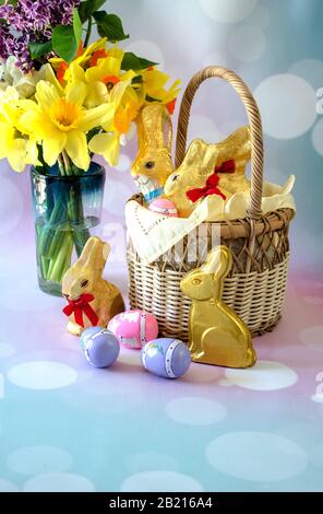 Un grazioso cestino di Pasqua è riempito di coniglietti di cioccolato e fiori primaverili siedono accanto ad esso, insieme con più caramelle e uova decorative Foto Stock