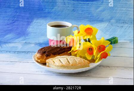 Il piatto con pasticcini di fantasia è decorato con un bouquet luminoso di narcisi e una tazza colorata piena di caffè Foto Stock