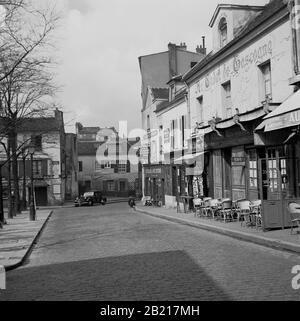 1950s, Parigi, Francia, strada acciottolata con ristoranti accanto A Place du Tertre, una piazza nella zona di Montmartre della città parigina, famosa per i suoi artisti di strada e la chiesa, Sacre Coeur. Tavoli e sedie sul marciapiede fuori dai ristoranti francesi visti nella foto, 'la Mere Catherine' e 'Hu Cadet de Gascogne'. Foto Stock