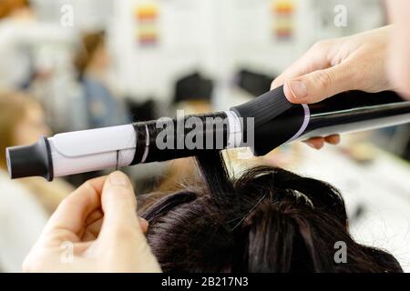 Capelli stylist arricciatura capelli primo piano. Parrucchiere che fa acconciatura a marrone donna capelli lunghi in salone di bellezza. Cura professionale dei capelli, Parrucchiere Foto Stock
