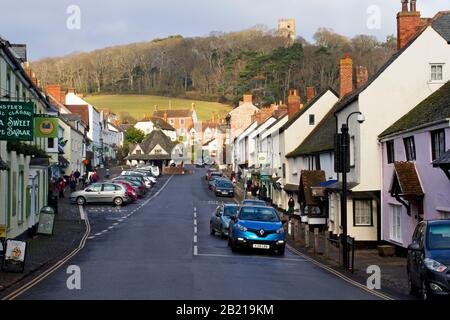 Una vista lungo Dunster High Street nel Somerset, Inghilterra che mostra il Mercato Dei Filati alla fine e la Conygar Tower visibile su una collina in lontananza. Foto Stock