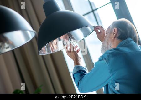 Uomo anziano concentrato che cambia una lampadina da solo Foto Stock