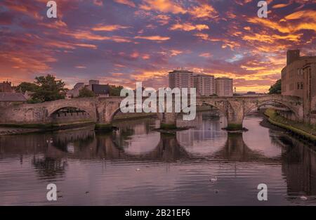 Lo storico Ponte Vecchio di Ayr in Scozia che attraversa il fiume Ayr e uno spettacolare tramonto rosso brillante sulla città. Foto Stock