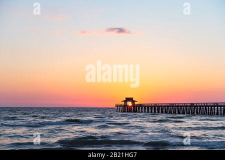 Napoli, Florida vibrante tramonto giallo rosso nel golfo del Messico con sole all'interno incorniciatura molo molo molo in legno molo all'orizzonte e silhouette scura oceano onde larghe Foto Stock