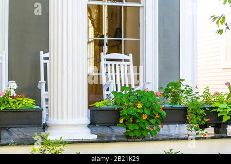 Storico quartiere dei giardini a New Orleans, Louisiana con patio giardino piante verdi fiori su colonna bianca anticellum e sedie a dondolo sulla vecchia strada Foto Stock