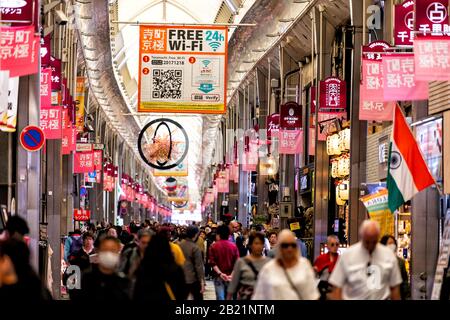 Kyoto, Giappone - 17 aprile 2019: Molte persone affollano turisti che camminano nei negozi del mercato Nishiki arcade con cartelli appesi Foto Stock