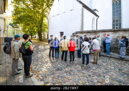 Un gruppo di tour fa una pausa per ascoltare una guida turistica su una strada acciottolata nel centro storico medievale di Tallinn Estonia. Foto Stock