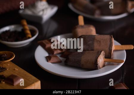 Gelato al cioccolato e biscotto su una tazza di ceramica bianca con fondo di legno marrone con pezzi di cioccolato e biscotti Foto Stock