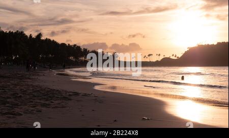 Lavaggio a onde morbide su una spiaggia di mare topica al tramonto. Vicino onde calme del mare sulla spiaggia di sabbia al tramonto. Riflessione del sole in acqua di mare. Foto Stock