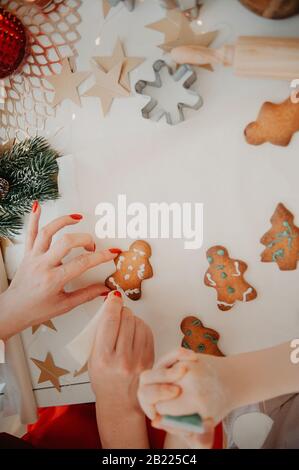 mani di mamma e bambino tagliano i biscotti dalla pasta usando stampi metallici, su carta da forno, su un tavolo bianco con decorazioni da stelle di carta Foto Stock
