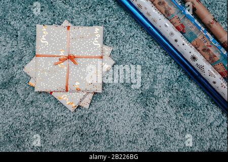 busta regalo bianca con un nastro d'oro su un soffice tappeto blu con un'alta pila attorno alla carta da imballaggio in rotoli per l'agugliatura Foto Stock