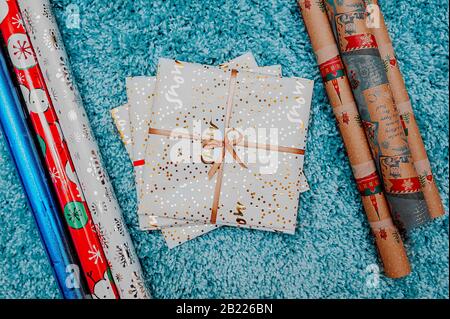 busta regalo bianca con un nastro d'oro su un soffice tappeto blu con un'alta pila attorno alla carta da imballaggio in rotoli per l'agugliatura Foto Stock