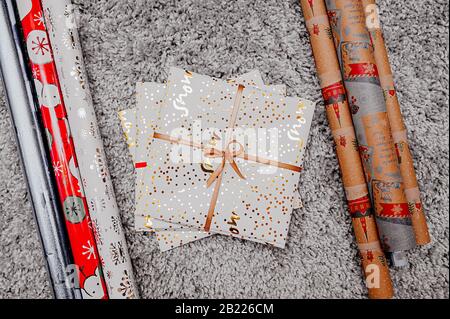 busta regalo bianca con un nastro d'oro su un soffice tappeto grigio con un'alta pila attorno alla carta da imballaggio in rotoli per l'agugliatura Foto Stock