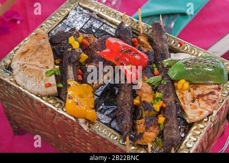 Pasto a la carte con griglieria mista a base di carne al barbecue su piastra calda in un ristorante con tovaglia viola Foto Stock