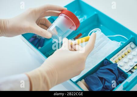 Donna in guanti tenere lancet per il sangue e coppa di prova. Confezione per la medicina domestica con articoli medici. Concetto di sanità e medicina. Foto Stock