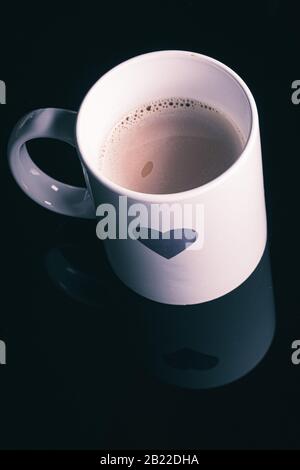 Forma del cuore dipinta su una tazza bianca per la mattina su uno sfondo nero Foto Stock