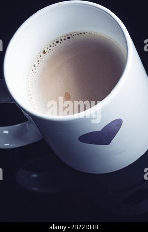 Forma del cuore dipinta su una tazza bianca per la mattina su uno sfondo nero Foto Stock