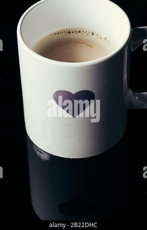 Forma del cuore dipinta su una tazza bianca per la mattina su uno sfondo nero Foto Stock