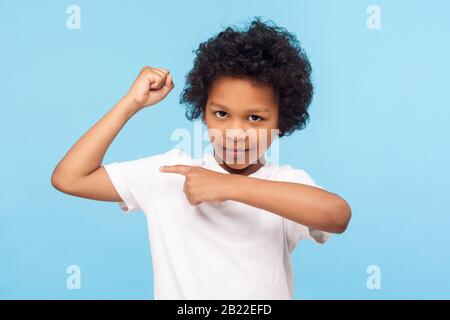 Guarda il mio muscolo, sono forte. Ritratto di adorabile ragazzino in T-shirt che punta al bicipite, sensazione di forza potente e sicuro di sé, mostrando forza. Io Foto Stock