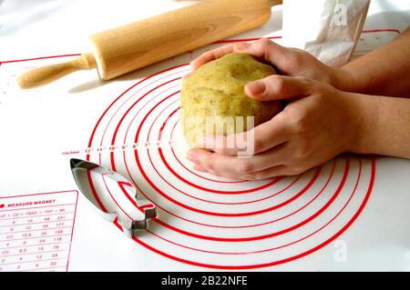 cucina e concetto domestico, primo piano di mani femminili che fanno i biscotti dall'impasto fresco nel paese, la taglierina del biscotto a forma di carota sul tappetino di silicone. legno Foto Stock