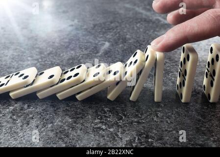 primo piano della mano maschile che impedisce che la linea di piastrelle domino si rovesci e cada, prevenzione dell'effetto domino e arresto del concetto di catena di eventi Foto Stock