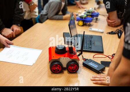 Robotica, robot fai da te a quattro ruote con antenna, laptop sul tavolo, persone riunite in giro, meeting tecnico, presentazione. Ingegneria meccanica semplice Foto Stock