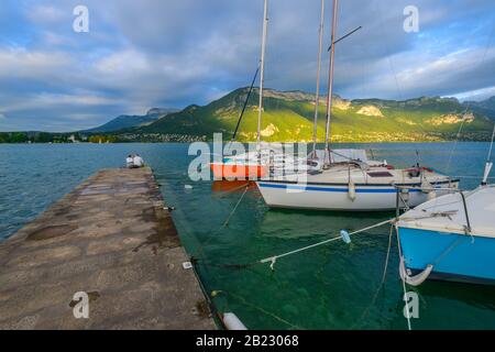 Barche a vela ormeggiate sul lago di Annecy, uno dei laghi più grandi in Francia e più puliti in Europa, e una coppia seduto e guardando il lago. Foto Stock