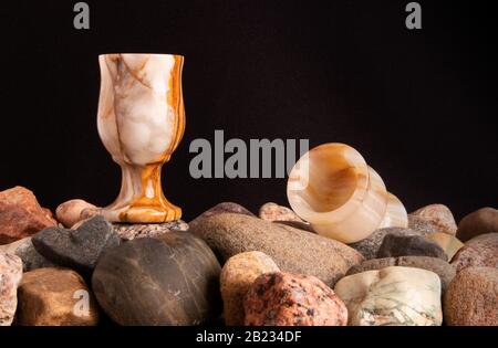 Ancora vita con due bicchieri onice su un mucchio di ghiaia e conchiglie contro il tessuto nero Foto Stock