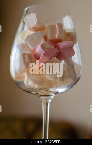 Bicchiere di vino con mini marshmallows. Marshmallow multicolore in un calice di vetro. Vista laterale. Messa a fuoco selettiva. Sfondo sfocato. Foto Stock