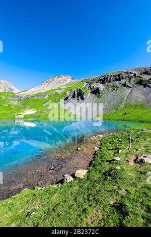 Vista verticale ad ampio angolo con persona di turchese Lago di ghiaccio vicino a Silverton, Colorado su cima rocciosa montagna picco e neve nell'agosto 2019 estate Foto Stock