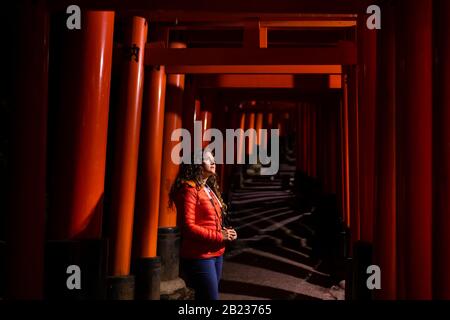 Kyoto, Giappone con giovane donna caucasica in piedi da Fushimi Inari rosso santuario torii porte nel parco di notte con lanterne illuminazione per percorso Foto Stock