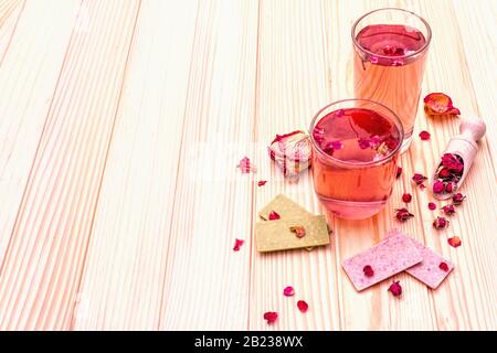 Rinfresco estivo tè da fiori di rose. Bevanda fredda in vetro con lampone e cioccolato al tè matcha, petali rosa. Su sfondo di legno, copia spazio Foto Stock