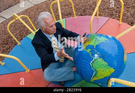 Unentschlossener Mann sitzt vor Weltkugel und schmiedet Reiseplaene, MR: Si Foto Stock
