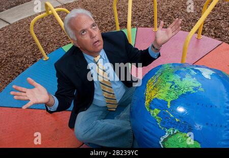 Unentschlossener Mann sitzt vor Weltkugel und schmiedet Reiseplaene, MR: Si Foto Stock