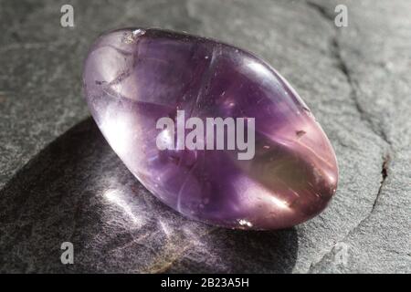 Ametrina tumbled ghiaia su sfondo grigio ardesia, illuminato dal sole Foto Stock