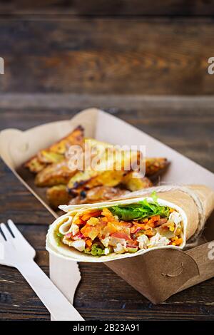 Delizioso sandwich shawarma con pollo e patate su sfondo di legno Foto Stock