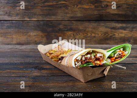 Delizioso sandwich shawarma con pollo e patate su sfondo di legno Foto Stock