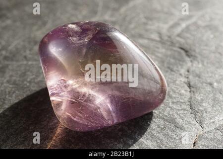 Ametrina tumbled ghiaia su sfondo grigio ardesia, illuminato dal sole Foto Stock