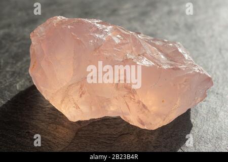 Ciottoli di quarzo rosa non tagliati e crudi su una piastrella di ardesia grigia, illuminata dal sole Foto Stock