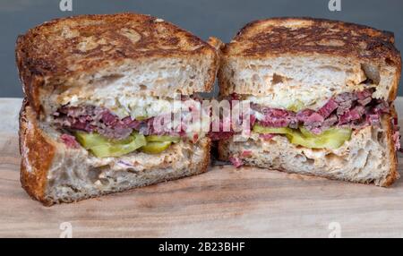 Primo piano di Salt Beef Reuben Sandwich. Pastrami, pane tostato con pasta di sourdough, brisket di manzo, insalata di cavolo e sottaceti su tavole di legno. Profondità di campo bassa Foto Stock