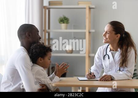 Medico pediatra sorridente che consulta il padre americano africano circa la salute del figlio Foto Stock