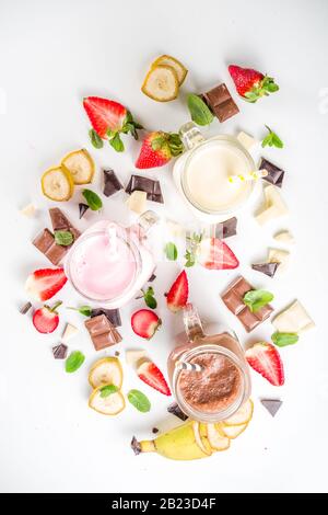 Tre vasetti da muratore con milkshake o frullato. Colazione estiva sana, pranzo bevande - banana, cioccolato e fragole milkshake su backgroun in legno Foto Stock