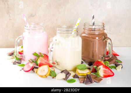 Tre vasetti da muratore con milkshake o frullato. Colazione estiva sana, pranzo bevande - banana, cioccolato e fragole milkshake su backgroun in legno Foto Stock