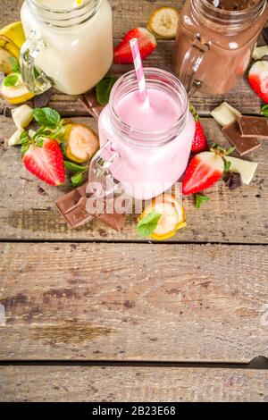 Tre vasetti da muratore con milkshake o frullato. Colazione estiva sana, pranzo bevande - banana, cioccolato e fragole milkshake su backgroun in legno Foto Stock